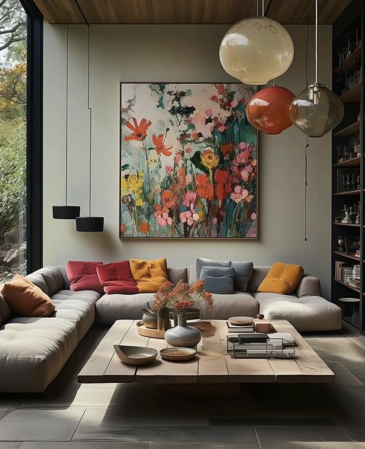 Modern living room with large floral painting, cozy sectional sofa, colorful cushions, wooden coffee table, and hanging glass lights.