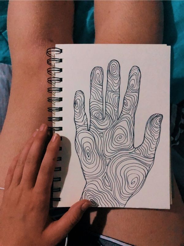 Sketchbook page showing a hand drawing with intricate swirling lines, laid on a person's lap for an artistic and creative touch.