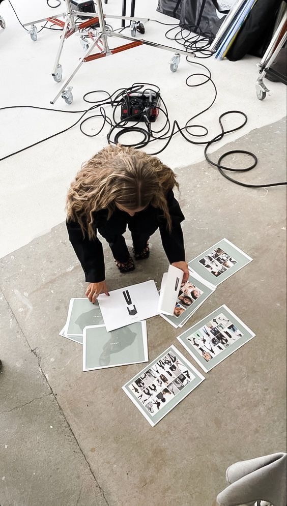 _ 7 Person reviews fashion layouts on a studio floor, surrounded by photography equipment and cables. Creative workspace scene. | Sky Rye Design Person reviews fashion layouts on a studio floor, surrounded by photography equipment and cables. Creative workspace scene.