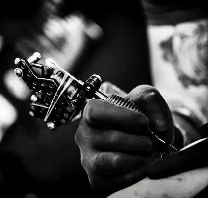 Tattoo artist holding a tattoo machine, creating intricate design, black and white close-up shot, emphasizing craftsmanship and detail.