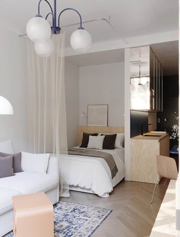Modern studio apartment with open layout, featuring a cozy bed, elegant pendant lights, stylish sofa, and a small kitchenette.
