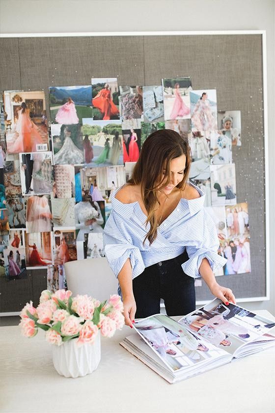 Fashion designer reviews inspiration board and magazine in creative workspace with pink roses in foreground.