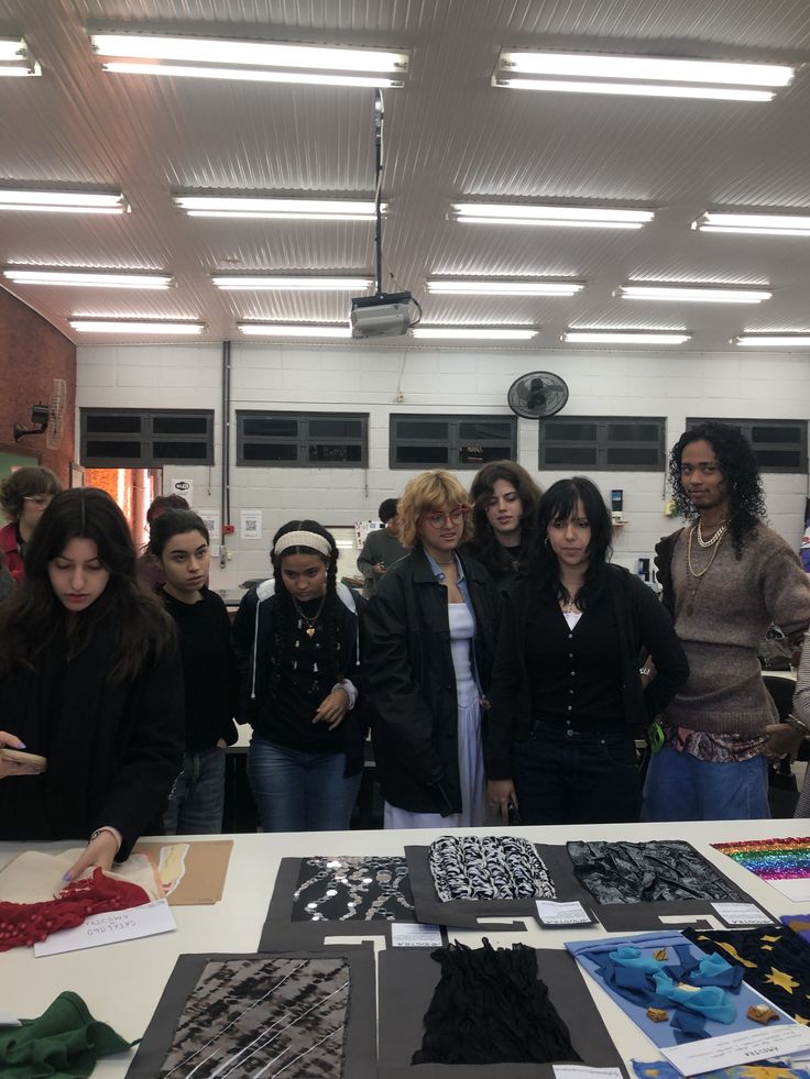 A group of people examining textile designs on a table in a brightly lit room with a modern ceiling.