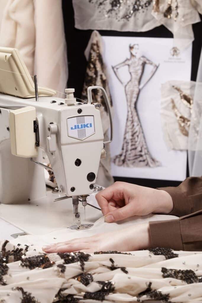 _ 7 Sewing elegant designer gown with a sewing machine; fabric embellished with sequins in a fashion studio. | Sky Rye Design Sewing elegant designer gown with a sewing machine; fabric embellished with sequins in a fashion studio.