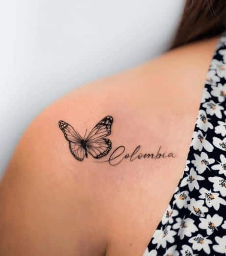 70 Meaningful Small Butterfly Tattoo Ideas To Try In 2023 Tattoo of a butterfly and the word Colombia on a shoulder in floral dress. | Sky Rye Design Tattoo of a butterfly and the word Colombia on a shoulder in floral dress.
