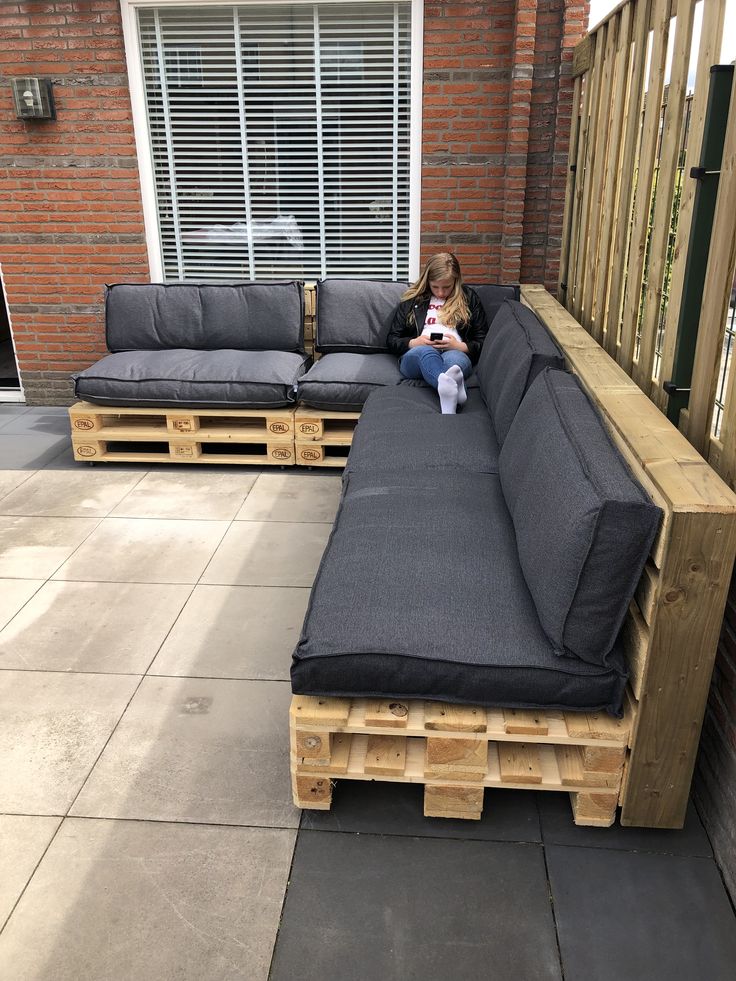 76d5d595411fb845e59cf6393506a250 Girl relaxing on DIY outdoor pallet sofa with gray cushions, using phone in a modern patio setting. Cozy and sustainable furniture idea. | Sky Rye Design Girl relaxing on DIY outdoor pallet sofa with gray cushions, using phone in a modern patio setting. Cozy and sustainable furniture idea.