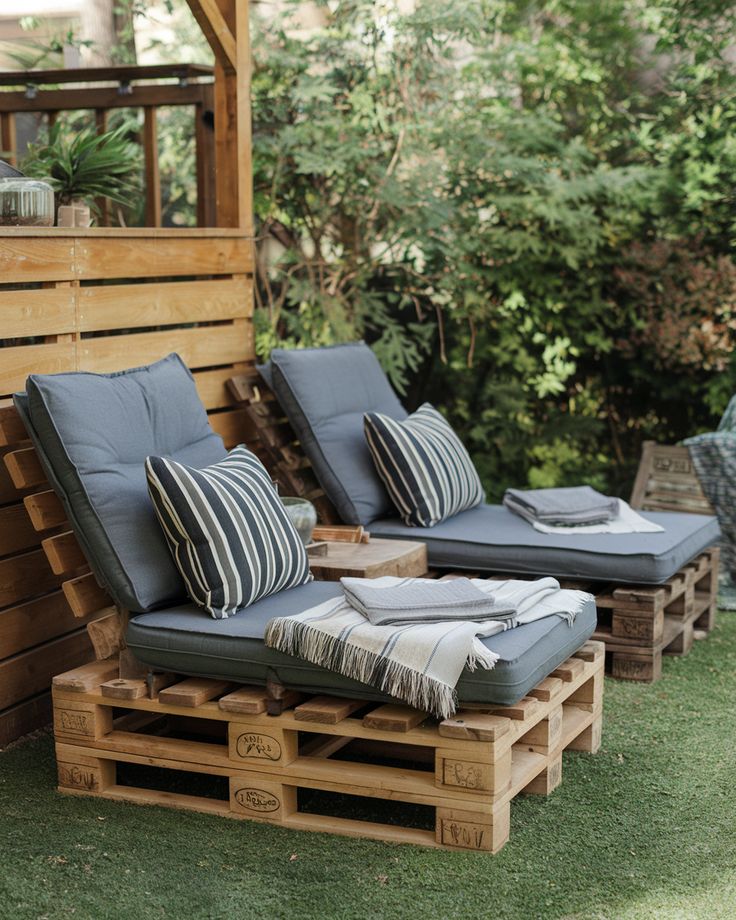 76f6d29bf67ac46ef72c3a1665e9f9d6 Cozy outdoor seating area with pallet loungers, blue cushions, and striped pillows on a grass lawn, surrounded by greenery. | Sky Rye Design Cozy outdoor seating area with pallet loungers, blue cushions, and striped pillows on a grass lawn, surrounded by greenery.