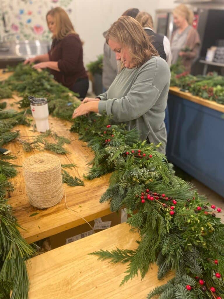 7877ed3ad440804cfcd3902678a08d80 Women crafting festive holiday wreaths with evergreen branches and red berries at a workshop, creating a warm and creative atmosphere. | Sky Rye Design Women crafting festive holiday wreaths with evergreen branches and red berries at a workshop, creating a warm and creative atmosphere.