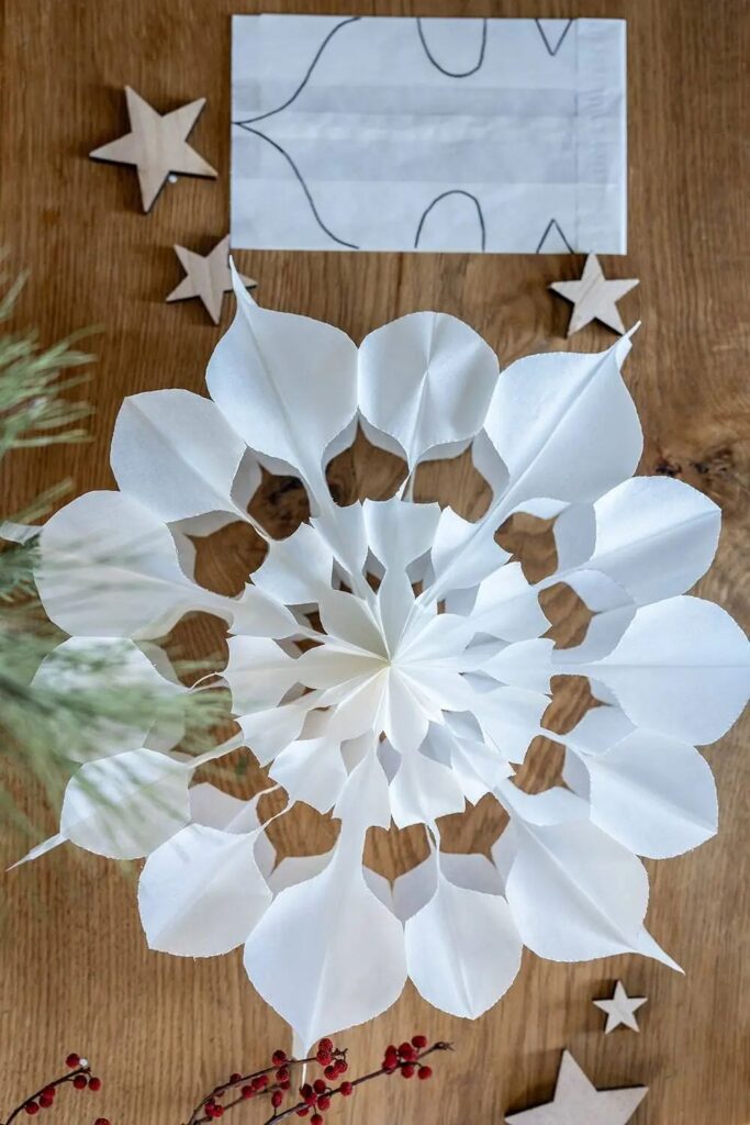 7e555c1f74cfc2a9a14e3752276b3695 Handmade paper snowflake with intricate design on wooden surface, surrounded by wooden stars and red berries for festive decoration. | Sky Rye Design Handmade paper snowflake with intricate design on wooden surface, surrounded by wooden stars and red berries for festive decoration.