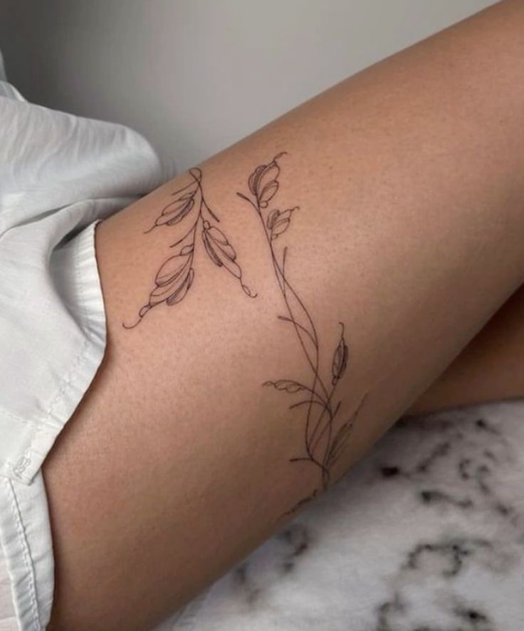 _ 8 Minimalist botanical tattoo on thigh featuring delicate leaf design, emphasizing elegance and simplicity, wearing white clothing. | Sky Rye Design Minimalist botanical tattoo on thigh featuring delicate leaf design, emphasizing elegance and simplicity, wearing white clothing.