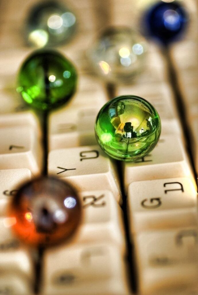 _ 8 Colorful glass marbles reflecting light, placed on computer keyboard keys, creating a vibrant and artistic office desk scene. | Sky Rye Design Colorful glass marbles reflecting light, placed on computer keyboard keys, creating a vibrant and artistic office desk scene.