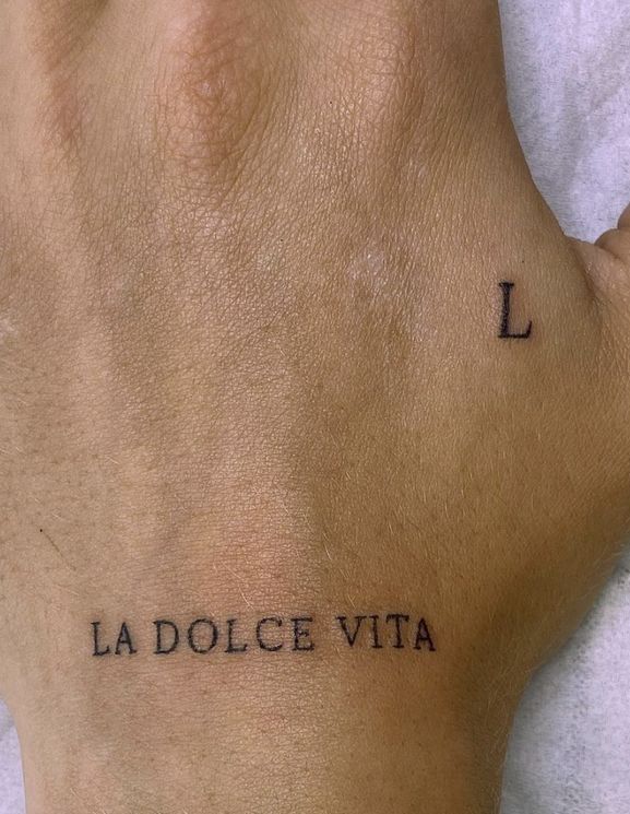Minimalist hand tattoo reading La Dolce Vita and L symbol on skin, reflecting a simple and elegant tattoo design.