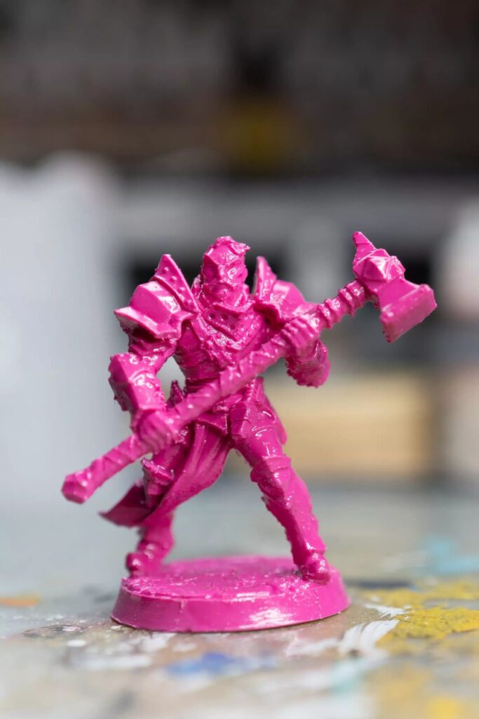 Pink 3D-printed warrior figurine holding an axe, showcasing intricate armor details on a blurred background.