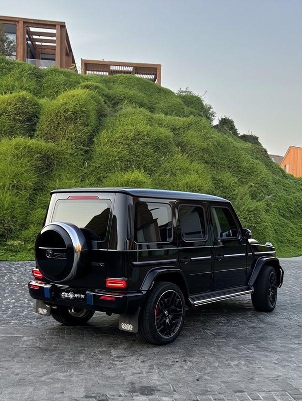 8f506394-284b-4bb7-8bf5-1a34c895308c Luxury black SUV parked on cobblestone driveway with green hillside and wooden structure in the background. | Sky Rye Design Luxury black SUV parked on cobblestone driveway with green hillside and wooden structure in the background.