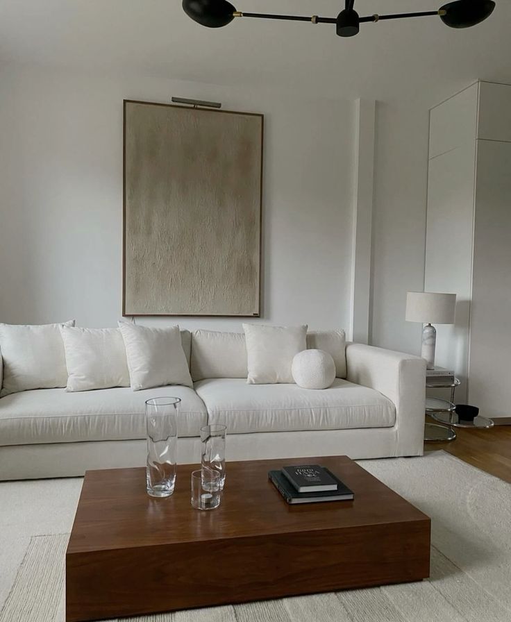 Minimalist living room with a white sofa, abstract wall art, wooden coffee table, and modern black chandelier.