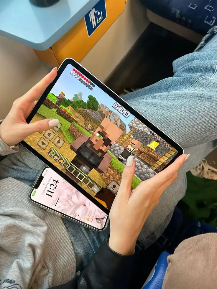 _ 9 Person playing Minecraft on a tablet while sitting on a train, with a smartphone displaying the time at 11:24 AM. | Sky Rye Design Person playing Minecraft on a tablet while sitting on a train, with a smartphone displaying the time at 11:24 AM.