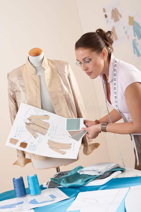 Fashion designer examining jacket sketch next to mannequin. Fabric swatches, measuring tape, and materials on table, planning clothing design.