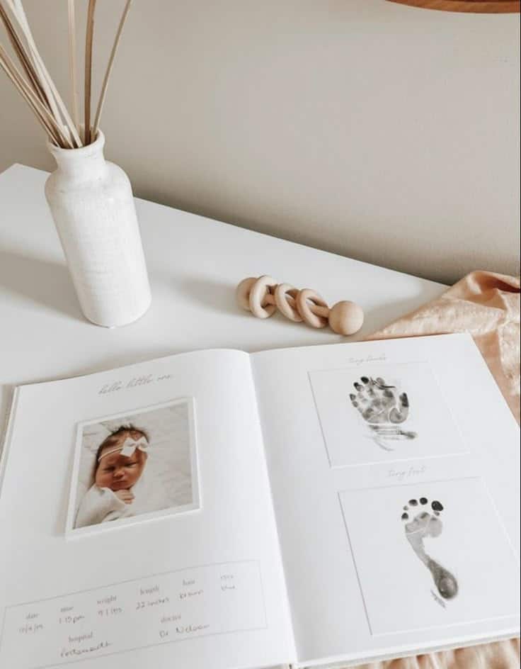9 Things to Include in Your Baby Keepsake Book Minimalist baby memory book with photo and handprint, footprint impressions. Decor includes a white vase and wooden beads on a table. | Sky Rye Design Minimalist baby memory book with photo and handprint, footprint impressions. Decor includes a white vase and wooden beads on a table.