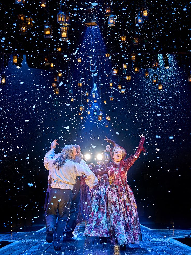 A Christmas Carol foto Manuel Harlan Actors dance joyfully on a snowy stage, surrounded by glowing lanterns and dramatic blue lighting, creating a festive atmosphere. | Sky Rye Design Actors dance joyfully on a snowy stage, surrounded by glowing lanterns and dramatic blue lighting, creating a festive atmosphere.