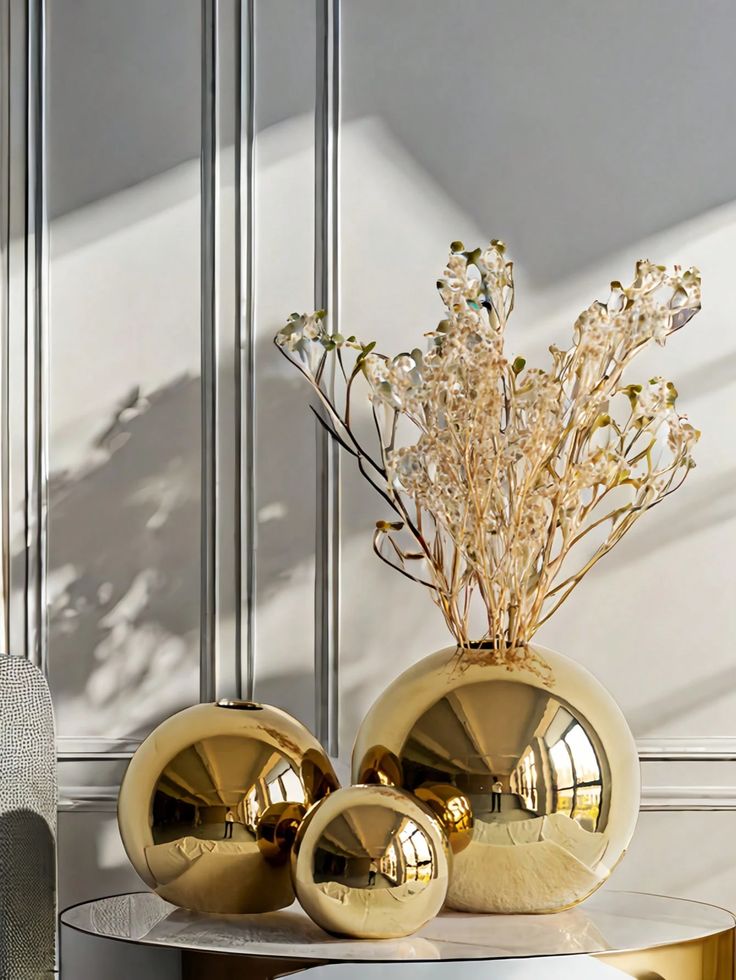 A Light Luxury Golden Spherical Vase Is Suitable Gold spherical vases with dried floral arrangements on a reflective marble table, set against a modern paneled wall in soft natural light. | Sky Rye Design Gold spherical vases with dried floral arrangements on a reflective marble table, set against a modern paneled wall in soft natural light.