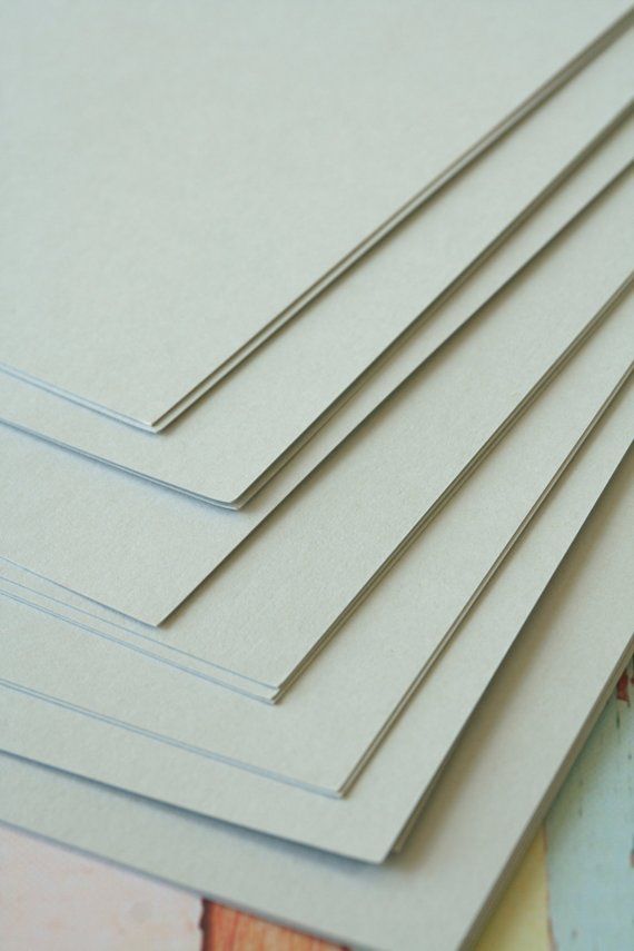 Stack of beige cardstock sheets on a table, ideal for crafts, printing, or invitations. High-quality, textured paper close-up.