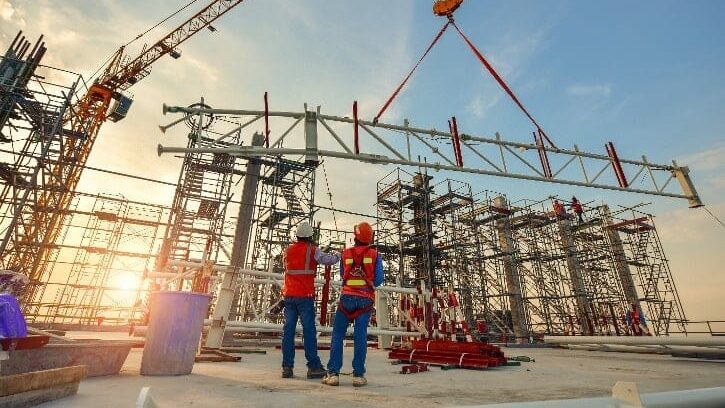 AdobeStock_222740403-1 Construction site at sunset with cranes lifting a steel beam, two workers in safety gear overseeing the process amidst scaffolding. | Sky Rye Design Construction site at sunset with cranes lifting a steel beam, two workers in safety gear overseeing the process amidst scaffolding.