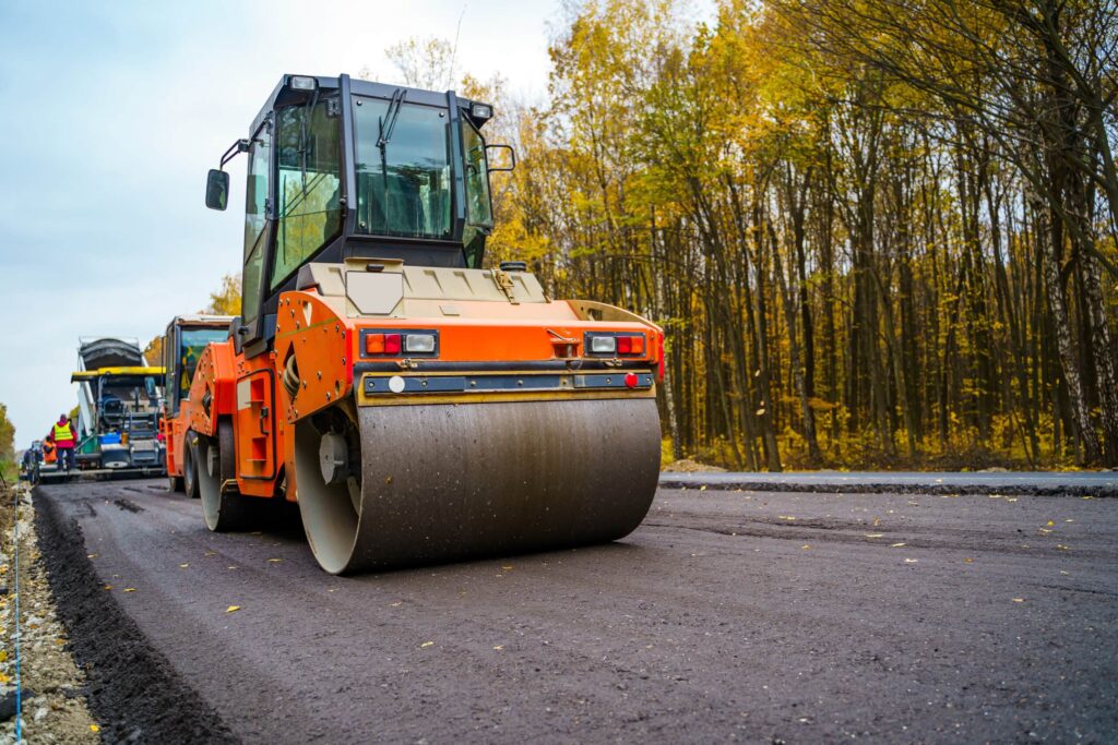 Road construction with an asphalt roller smoothing new pavement in a forest area during autumn.