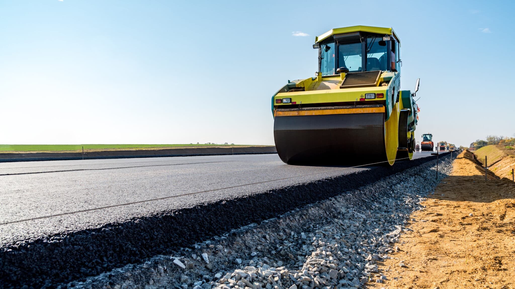 Road construction underway with a steamroller compacting fresh asphalt, creating a smooth surface for future travel.