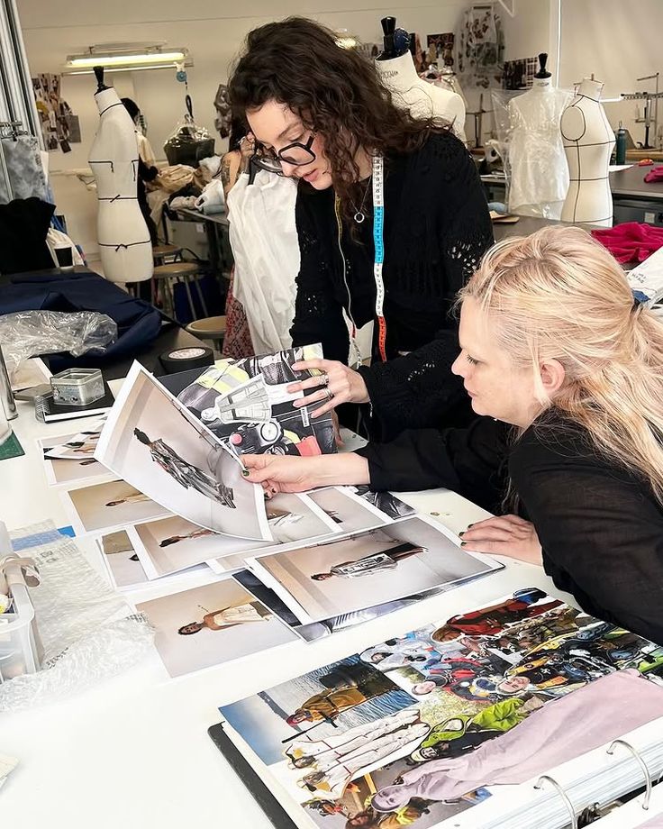 Fashion designers reviewing photo layouts in a creative studio, surrounded by mannequins and fabric samples.