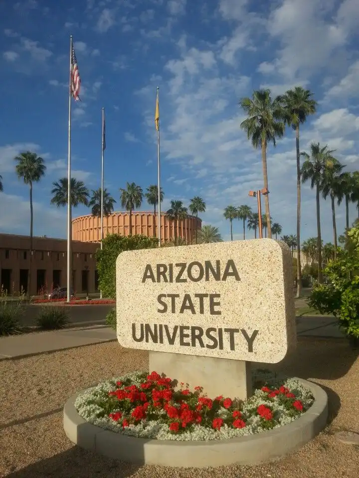 Arizona State University entrance sign with palm trees, blue sky, and vibrant red flowers, capturing a sunny campus atmosphere.