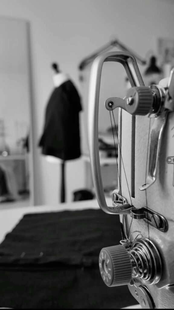 Atelier_vibes Close-up of an industrial sewing machine in a fashion studio, with fabric and a mannequin in the background, in black and white. | Sky Rye Design Close-up of an industrial sewing machine in a fashion studio, with fabric and a mannequin in the background, in black and white.