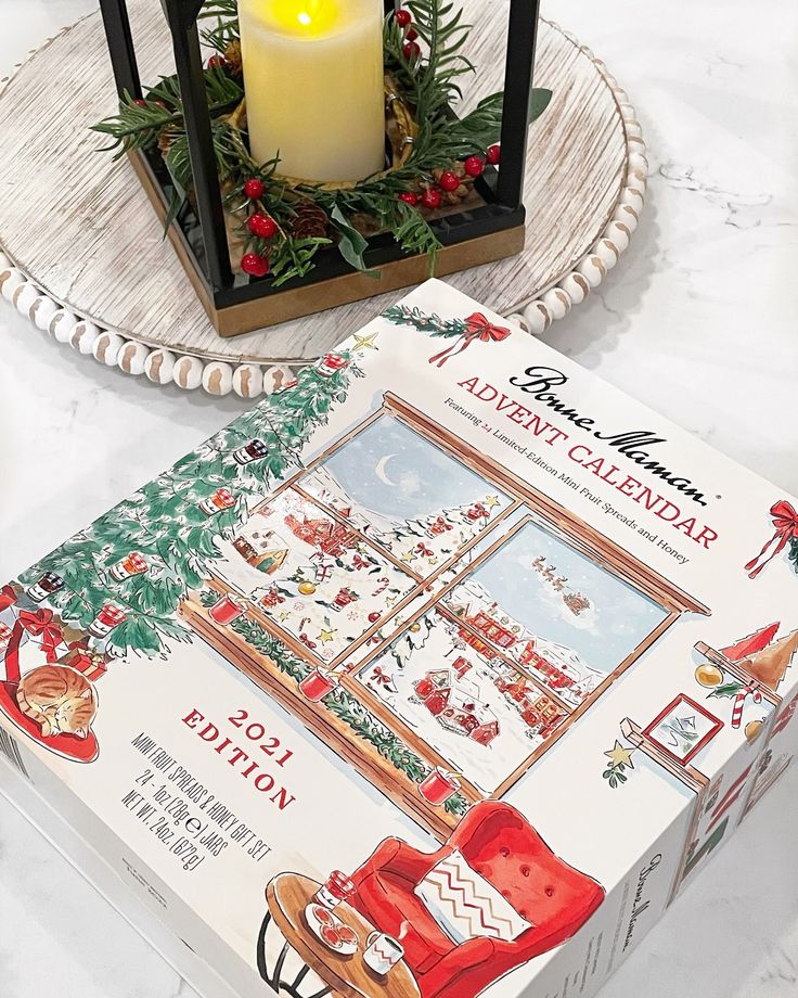 Festive advent calendar box with a cozy holiday scene beside a decorative candle centerpiece on a white wooden tray.