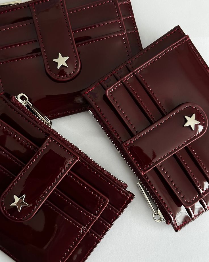 Burgundy wallets with star-shaped metal accents and multiple card slots, featuring sleek, glossy finishes and zipper compartments.