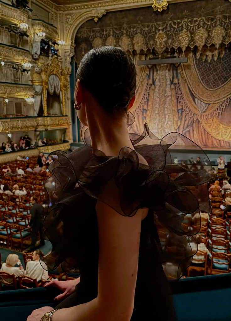Ballet evening Elegant woman in black dress at theater balcony, admiring ornate stage with luxurious decor and audience seated below. | Sky Rye Design Elegant woman in black dress at theater balcony, admiring ornate stage with luxurious decor and audience seated below.