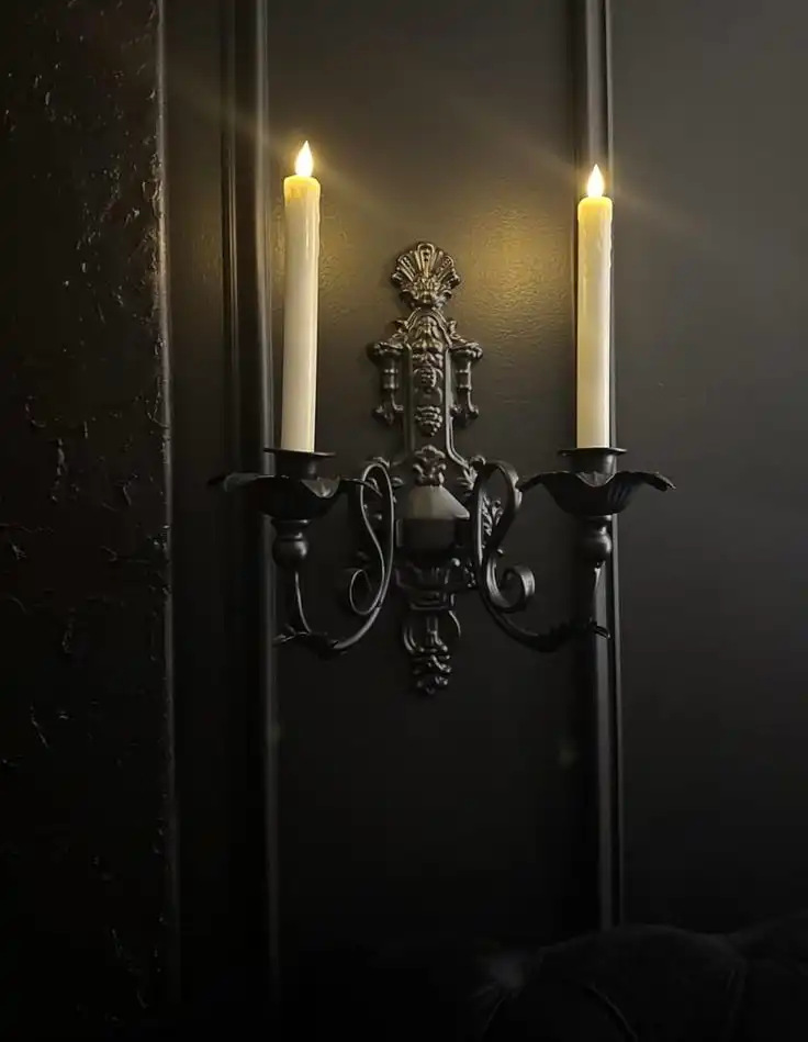 Elegant black wall sconce with two lit candles on a dark textured background, creating a warm and classic ambiance.