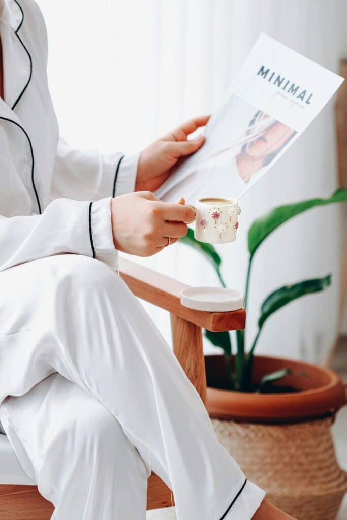 Building Micro-Habits_ Tiny Steps to a Better You Person in white pajamas sits with a magazine and a floral cup in hand, enjoying a cozy morning with plants and natural light. | Sky Rye Design Person in white pajamas sits with a magazine and a floral cup in hand, enjoying a cozy morning with plants and natural light.