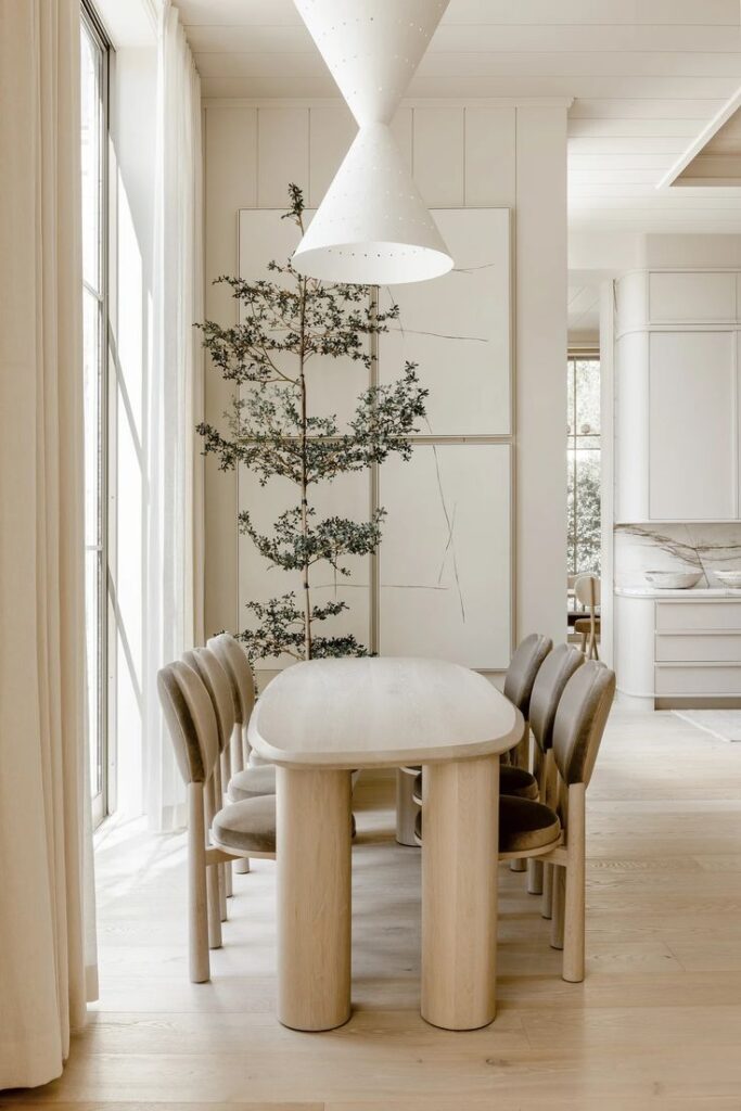 Minimalist dining room with a light wood table, stylish chairs, and contemporary pendant lights, complemented by a vertical plant accent.