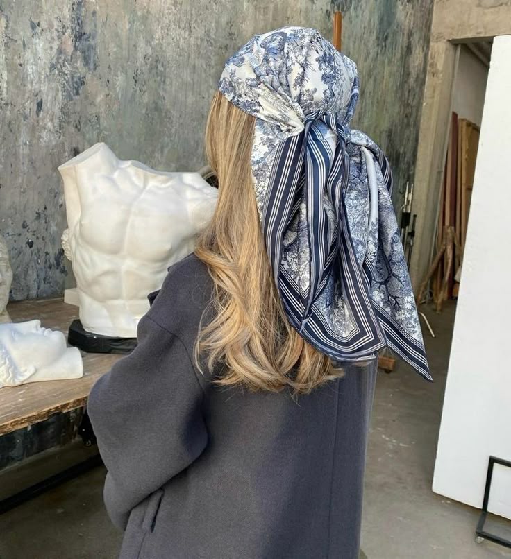 Cassandra Woman with long hair and patterned headscarf facing sculptures on a table in an art studio setting. | Sky Rye Design Woman with long hair and patterned headscarf facing sculptures on a table in an art studio setting.