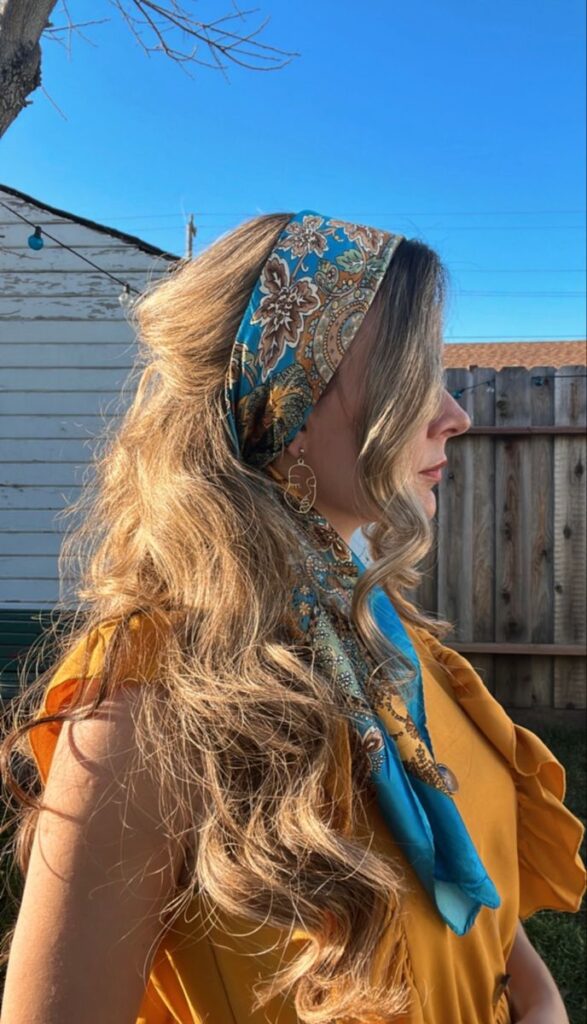 Ceren _ Hairstyles on Instagram_ _xoxo🦋🧡 hairstyles hairtutorials gossipgirl hairscarfs_ Woman in yellow dress with patterned blue headscarf, long wavy hair, profile view, outdoors, bright blue sky background. | Sky Rye Design Woman in yellow dress with patterned blue headscarf, long wavy hair, profile view, outdoors, bright blue sky background.
