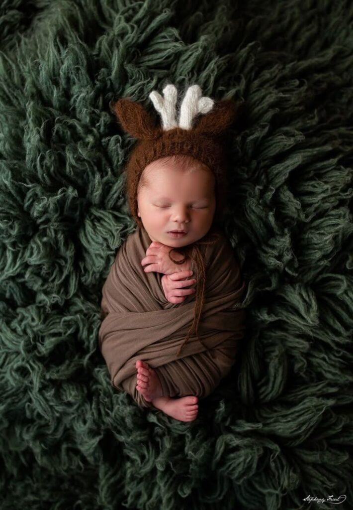 Christmas baby photography ideas _ Stephany Ficut Photography Sleeping baby wrapped in brown blanket, wearing a cute knitted hat with antlers, on a fluffy green background. | Sky Rye Design Sleeping baby wrapped in brown blanket, wearing a cute knitted hat with antlers, on a fluffy green background.