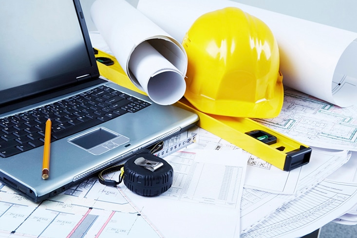 Civil-Engineering-now Laptop, yellow hard hat, blueprints, and measuring tools on a table, representing architecture and engineering work essentials. | Sky Rye Design Laptop, yellow hard hat, blueprints, and measuring tools on a table, representing architecture and engineering work essentials.