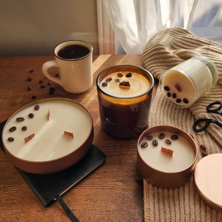 Cozy setting with coffee candles, a mug, and a knit blanket on a wooden table, perfect for a warm, inviting ambiance on a sunny day.