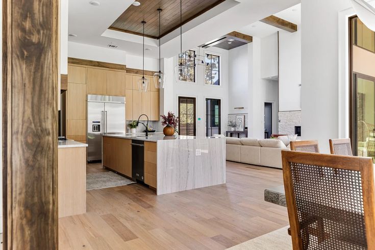 Modern open-concept kitchen and living area with high ceilings, wooden accents, marble countertops, and cozy seating in a bright, airy space.