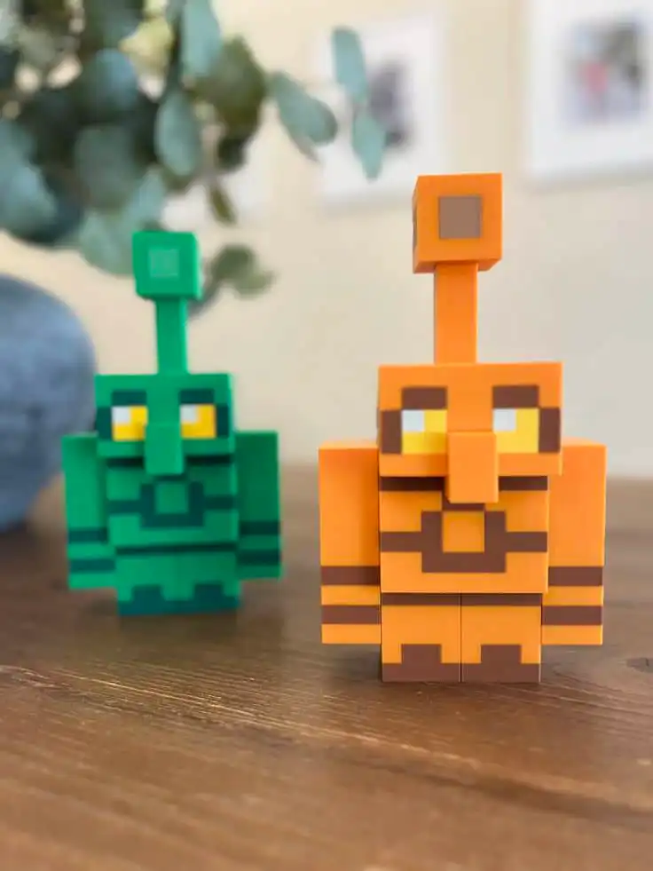 Copper Golem 3DThursday 3DPrinting Blocky orange and green toy figures with pixelated design on a wooden table, blurred plant background. | Sky Rye Design Blocky orange and green toy figures with pixelated design on a wooden table, blurred plant background.