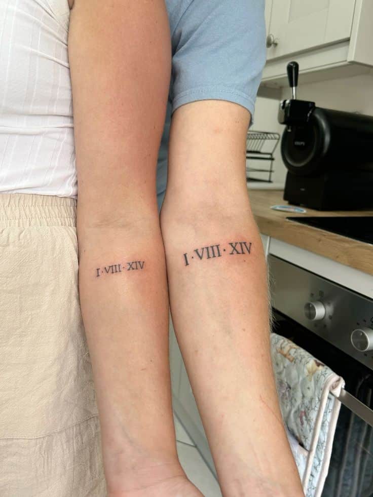 Couples matching tattoo Matching forearm tattoos with Roman numerals I-VIII-XIV, symbolizing a special date, on two arms in a cozy kitchen setting. | Sky Rye Design Matching forearm tattoos with Roman numerals I-VIII-XIV, symbolizing a special date, on two arms in a cozy kitchen setting.
