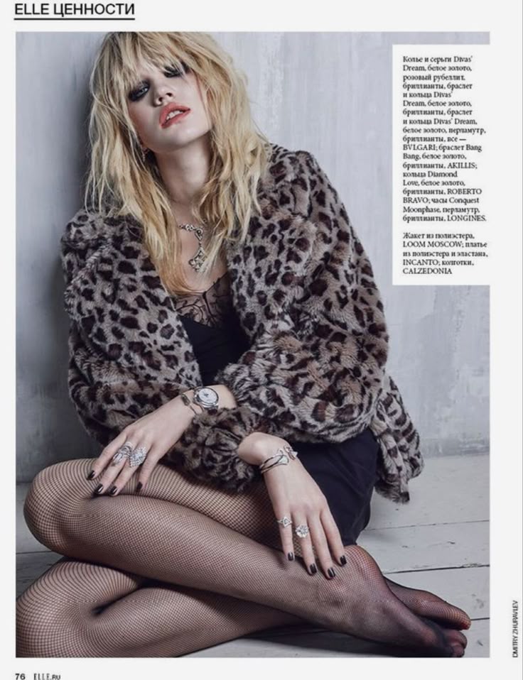 Fashionable woman in a leopard print coat, seated, wearing jewelry, fishnet stockings, and dark makeup for a chic, edgy look.