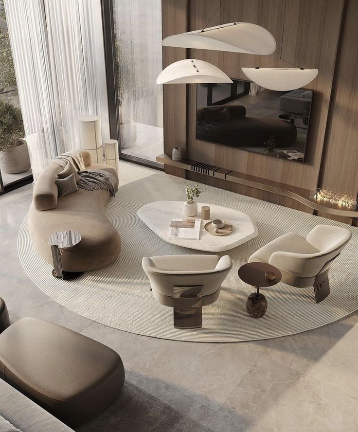 Modern, elegant living room with curved sofa, sleek chairs, and contemporary pendant lights above a circular rug. Neutral tones and large windows.