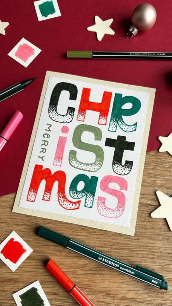 Create magical christmas cards 🎄🌟🤩 Festive Christmas card with colorful lettering, surrounded by markers and decorations on a wooden and red background. | Sky Rye Design Festive Christmas card with colorful lettering, surrounded by markers and decorations on a wooden and red background.