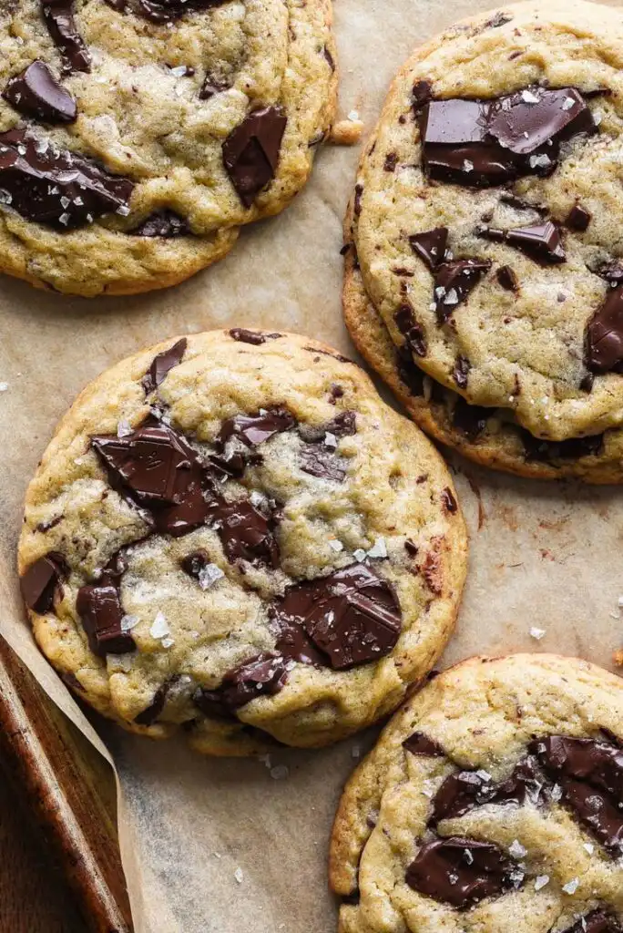 Freshly baked chocolate chunk cookies topped with sea salt flakes on parchment paper. Perfect dessert for chocolate lovers.