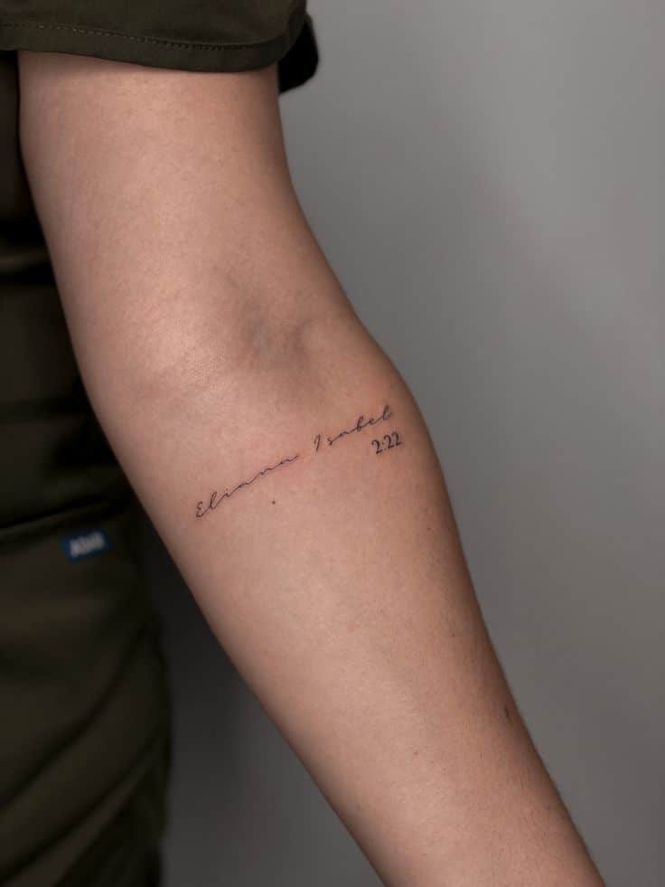 Script tattoo on forearm with cursive text and numbers, showcasing minimalist tattoo style with personalized touch.
